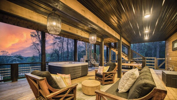A wooden deck with a hot tub, seating area, and a view of the forest. - Glass Cabin Retreat w/ Hot Tub, Sauna + Epic Views (Morganton)