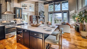 A spacious kitchen with a large island, built-in appliances, and a stone fireplace. - Glass Cabin Retreat w/ Hot Tub, Sauna + Epic Views (Morganton)