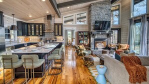 A spacious kitchen with a central island, a stone fireplace, and a high ceiling with exposed beams. - Glass Cabin Retreat w/ Hot Tub, Sauna + Epic Views (Morganton)