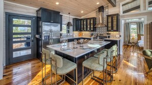 A modern kitchen with a large island, bar stools, and dark cabinetry. - Glass Cabin Retreat w/ Hot Tub, Sauna + Epic Views (Morganton)