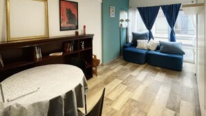 Un salon comprenant une table à manger, un ensemble de canapés, une bibliothèque et un tableau accroché au mur.