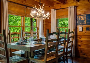 Ein Esszimmertisch mit Stühlen, einer Chandelierleuchtre und Blick auf Grünflächen.