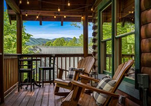 Eine Holzterrasse mit Adirondack-Stühlen und einem Tisch, mit Blick auf eine gebirgige Landschaft.