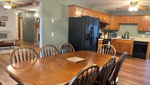 A dining area with a wooden table and chairs, a black refrigerator, wooden cabinets, and a kitchen area with appliances.