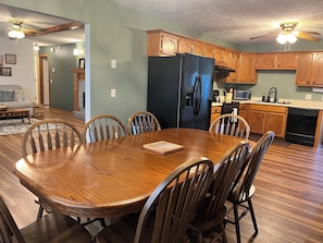 Comedor con mesa y sillas de madera, refrigerador negro, armarios de madera y zona de cocina con electrodomésticos.