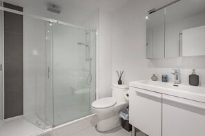 Uma casa de banho moderna com cabine de duche em vidro, sanita branca e lavatório com espelho e artigos de higiene pessoal.