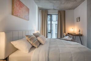 Quarto de hotel com cama, escrivaninha e janela com cortinas.