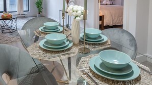 Un comedor con una mesa de vidrio dispuesta con platos verde azulado y cubiertos, rodeado de sillas grises.