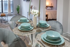 A dining area with a glass table set with teal plates and silverware, surrounded by grey chairs. - 1 bedroom old port- F1 Weekend (Montreal)