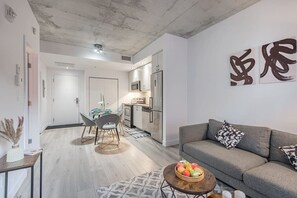 Uma sala de estar moderna com um sofá cinzento, uma mesa de jantar com cadeiras, uma área de cozinha e arte abstrata nas paredes.