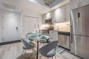 A modern kitchen with stainless steel appliances, a glass dining table, and grey chairs. - 1 bedroom old port- F1 Weekend (Montreal)