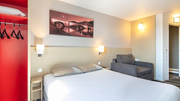Hotelkamer met een bed, een stoel, een nachtkastje, een wandlamp en een schilderij van een brug.