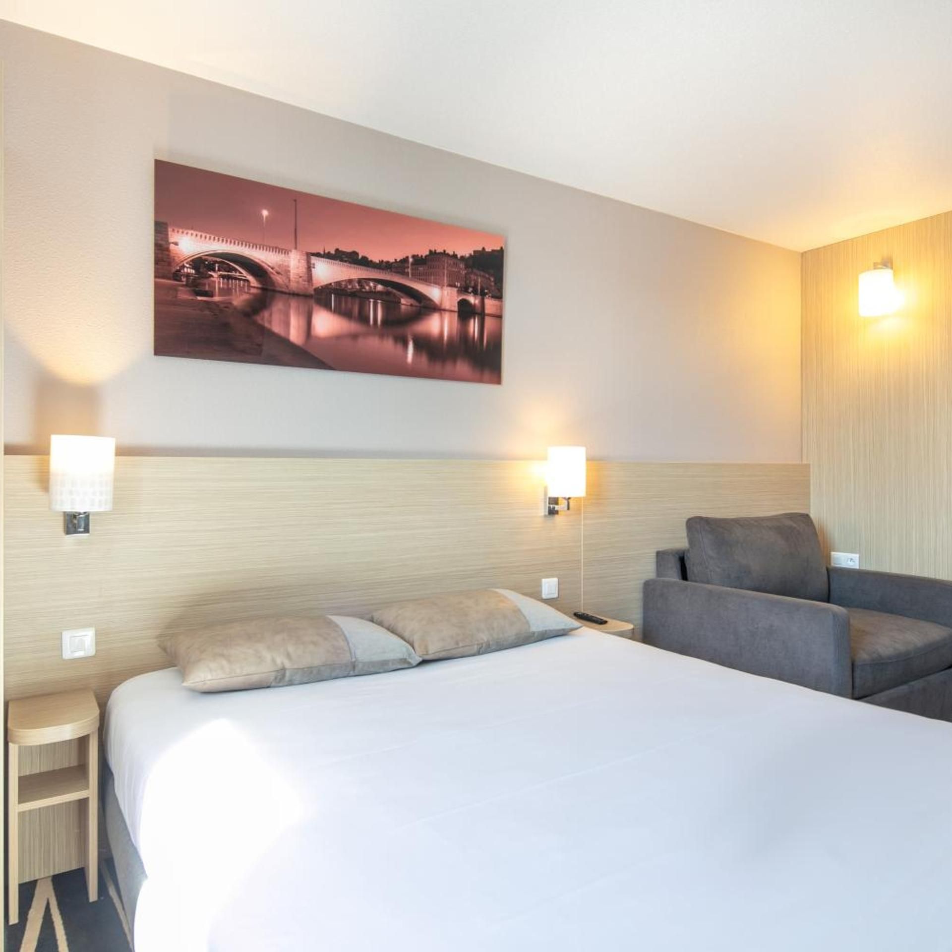 Ein Hotelzimmer mit einem Bett, einer Couch, zwei Wandlampen und einem großen Bild einer Brücke.