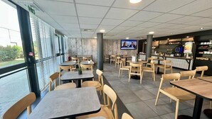 Een restaurant met tafels, stoelen, een televisiescherm en een toonbank met een menukaart.