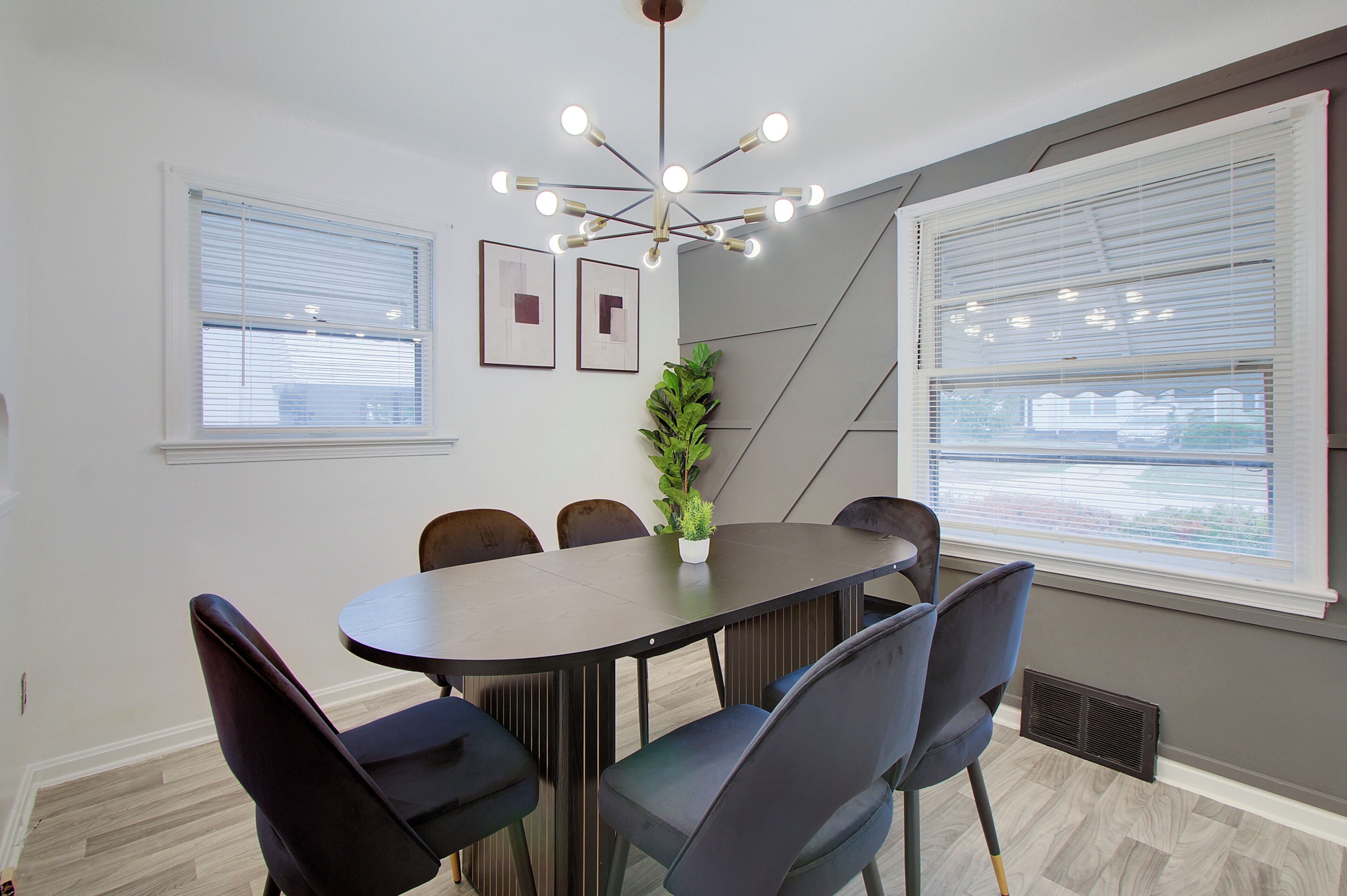 Comedor con una mesa redonda, seis sillas, una planta en maceta y dos ventanas con persianas.