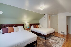 A hotel room with two beds, a nightstand with a lamp, a wooden floor, and a door leading to another room. - Pet-Friendly 3BR • Game Room • Near Hospitals (South Euclid)