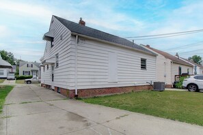 A single-story house with a brick foundation and white siding, a driveway, and a lawn. - Pet-Friendly 3BR • Game Room • Near Hospitals (South Euclid)
