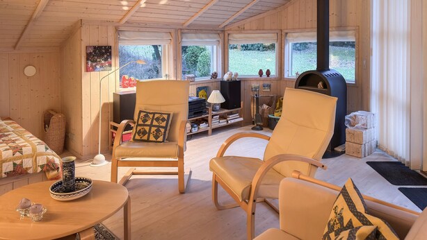 Indbydende hytteinteriør med trævægge, pejs, sofa og spisebord.