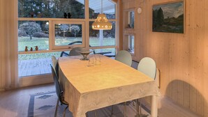 Spiseområde med et bord, stole, en hængende lampe og udsigt gennem store vinduer.