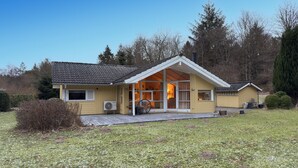 Et gult hus med overdækket veranda, en klimaanlæg og et lille skur.