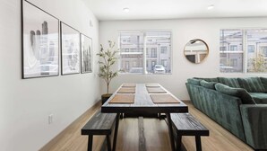 Uma sala de estar moderna com uma mesa de jantar de madeira, um sofá verde e quadros na parede.