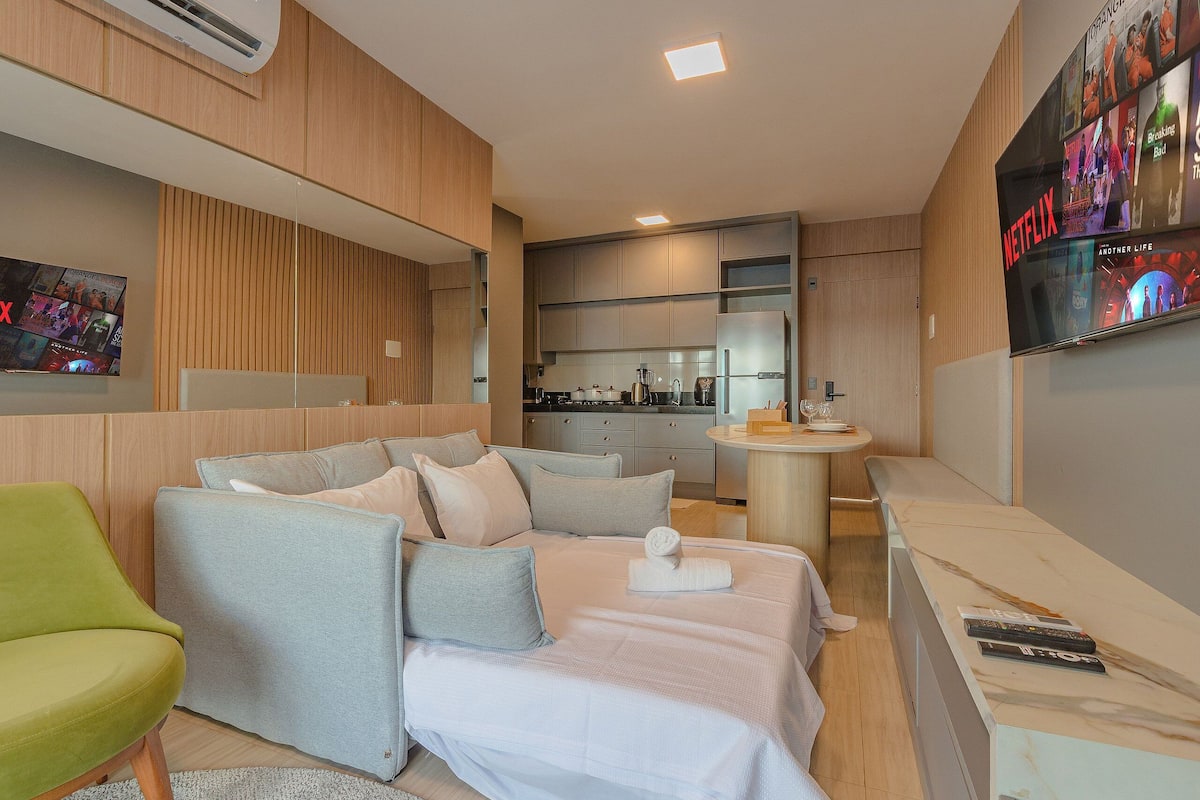 A modern hotel room with a sofa, a bed, a small kitchen area, and a TV displaying Netflix content.