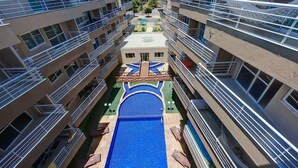 Ein mehrstöckiges Hotel mit Balkonen, einem zentral gelegenen Pool und Blick auf das Meer.