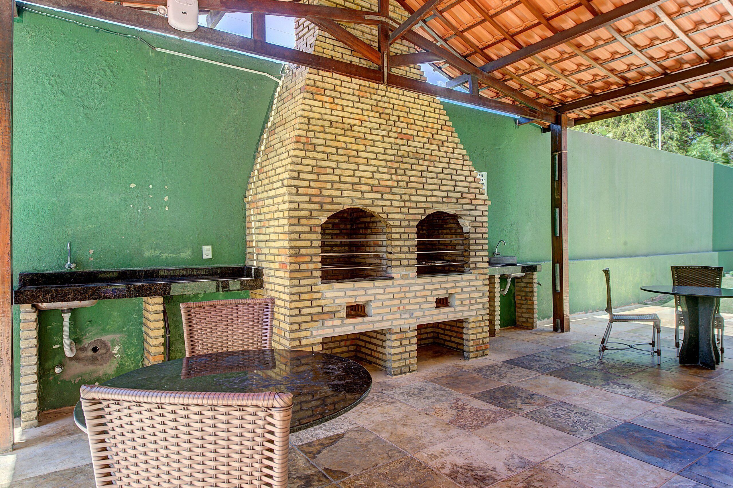 Patio esterno con forno a mattoni, sedie in vimini e un tavolo.