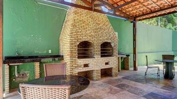 Patio esterno con forno a mattoni, sedie in vimini e un tavolo.
