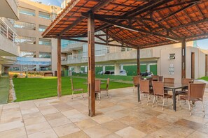 Un espace extérieur abrité avec des tables et des chaises, une piscine et, au fond, un immeuble à plusieurs étages.