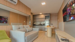 Ein modernes Wohnzimmer mit einer Couch, einem kleinen runden Tisch und einer Küchenzeile im Hintergrund.