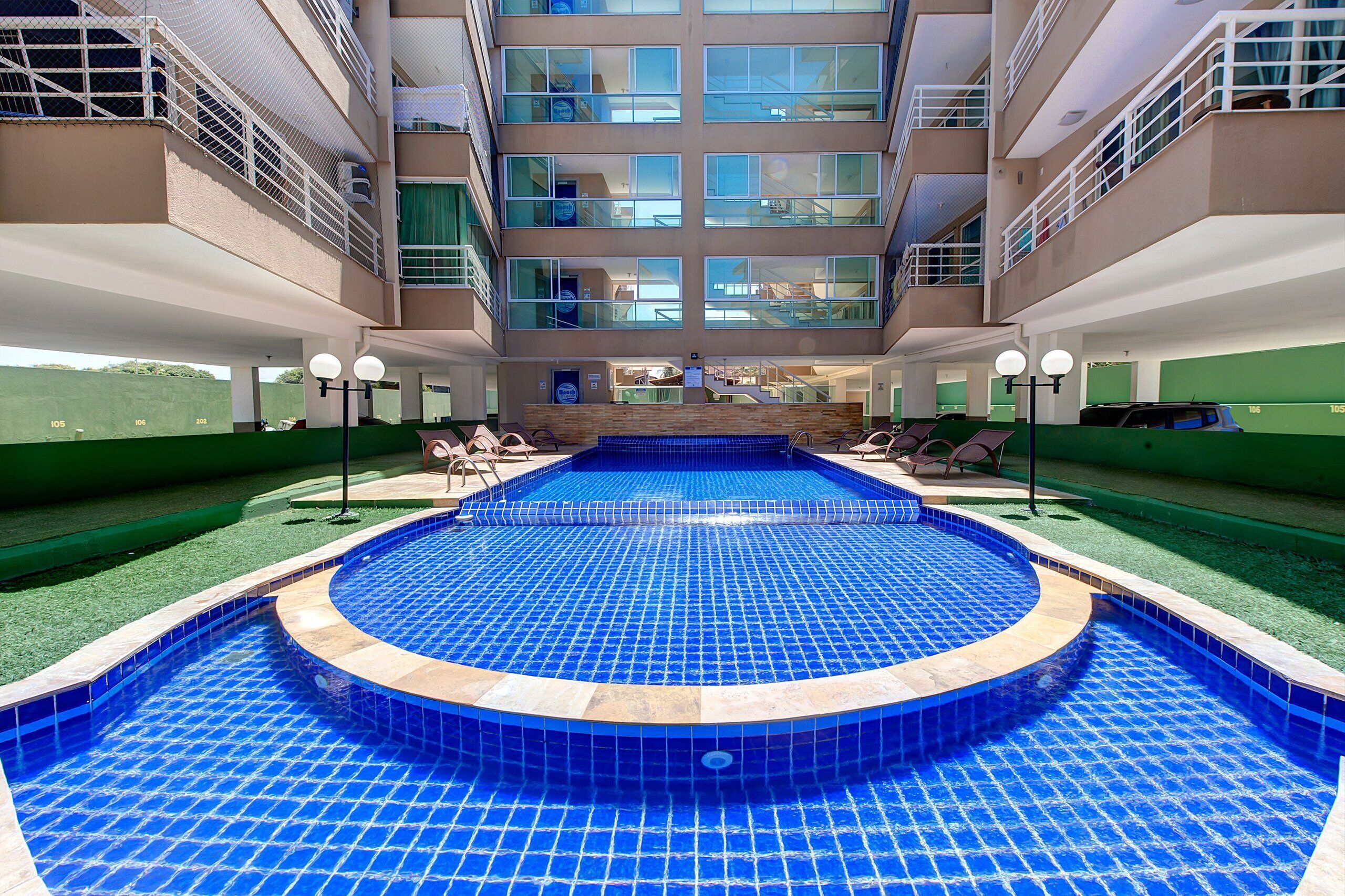 Un hotel con piscina central, varios balcones y vistas del entorno.