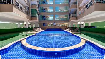 Un hotel con piscina central, varios balcones y vistas del entorno.