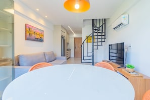 Una sala de estar moderna con una mesa de comedor de vidrio, un sofá, un televisor y una escalera.