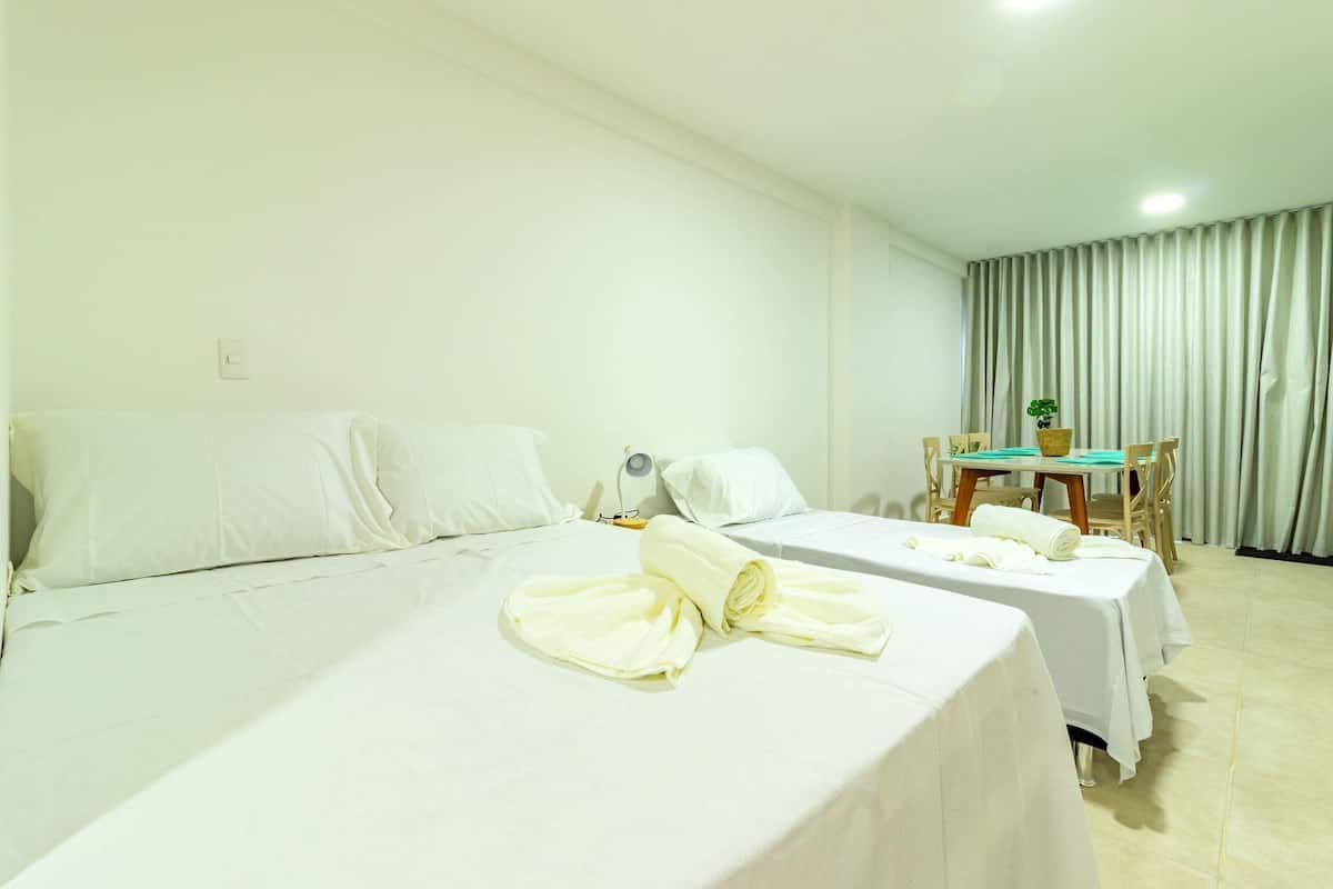 A hotel room with two beds, a table with chairs, a small table with a plant, and a curtain.
