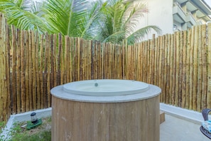 Un jacuzzi circular sobre una base de madera, rodeado por una valla de bambú, en un entorno exterior.