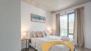 A modern bedroom with a bed, bedside lamps, a window with curtains, and a painting on the wall. - Chic 2BR in Old Port • Walk to Everything (Montreal)