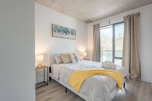 Ein modernes Schlafzimmer mit Bett, Nachttischlampen, einem Fenster mit Vorhängen und einem Bild an der Wand.