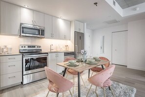 Eine moderne Küche mit Edelstahlgeräten, eine Essecke mit Holztisch und rosa Stühlen und ein heller, weißer Innenraum.