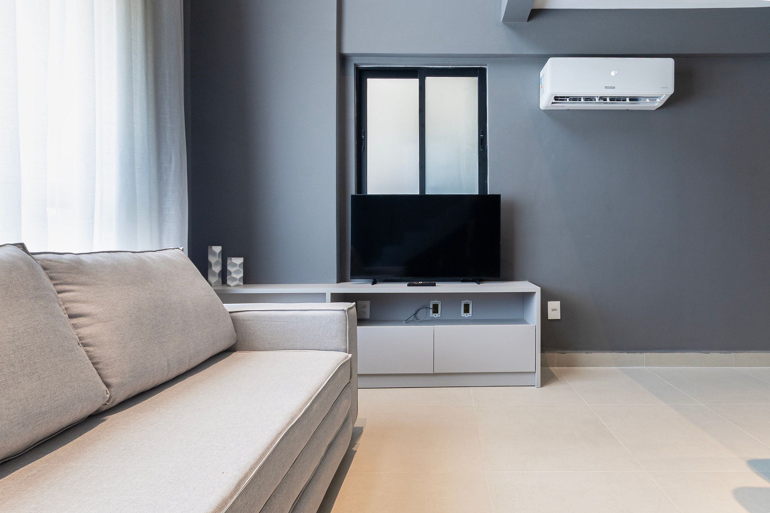 Een moderne woonkamer met een bank, een flatscreen televisie en een luchtverkoeler aan de muur.