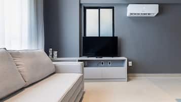 Een moderne woonkamer met een bank, een flatscreen televisie en een luchtverkoeler aan de muur.