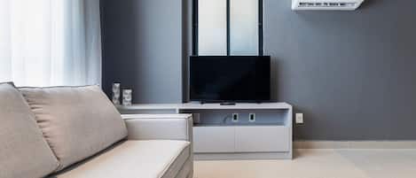 A modern living room with a sofa, a flat-screen TV, and a wall-mounted air conditioner.