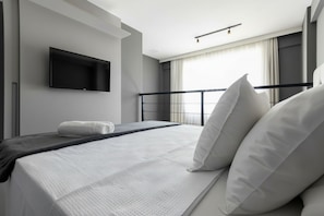Una habitación de hotel moderna con una cama, un televisor de pantalla plana en la pared, una ventana con cortinas y una barandilla de balcón.