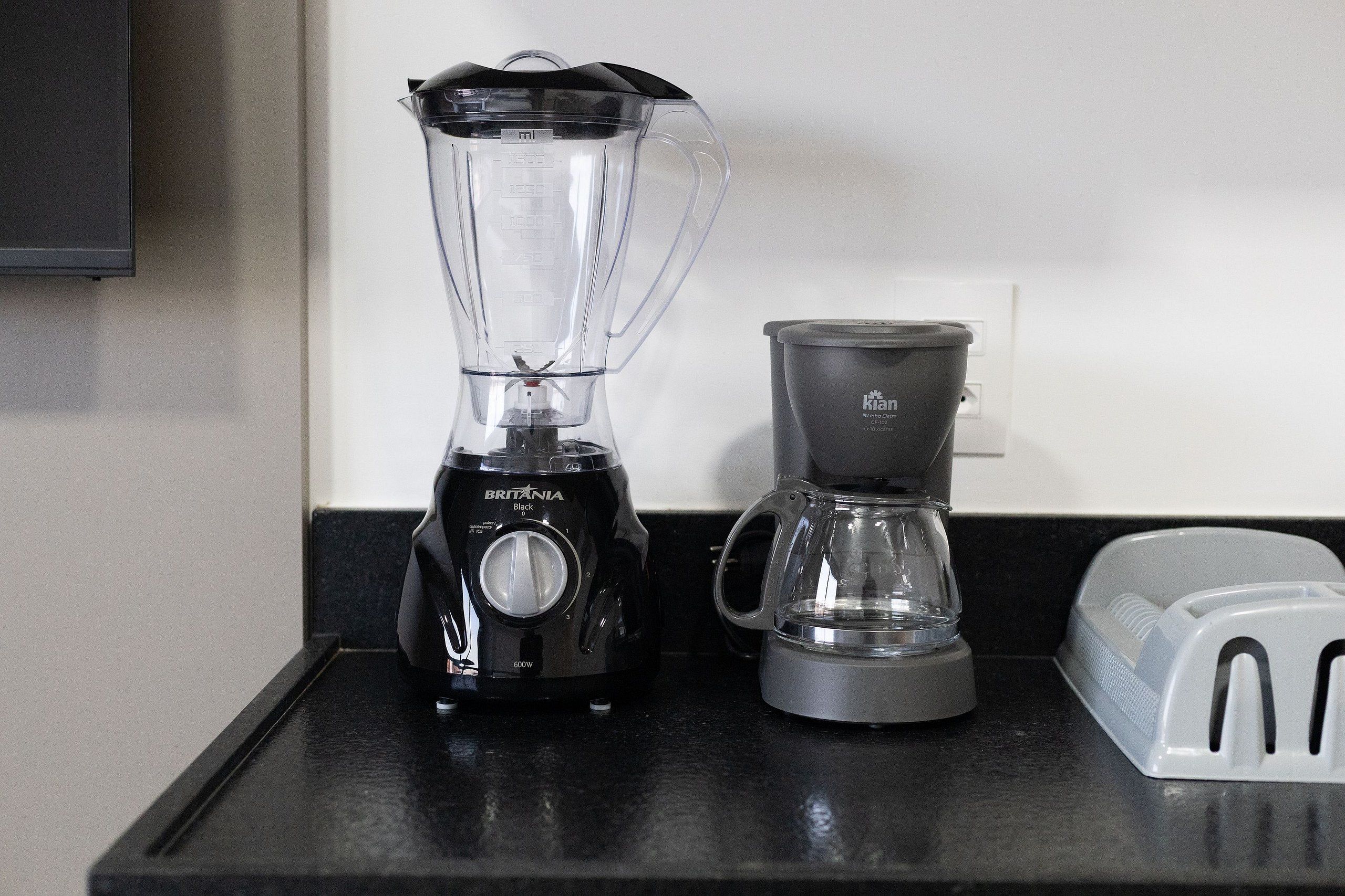 Una encimera de cocina con una licuadora negra, una cafetera gris y un tostador blanco.