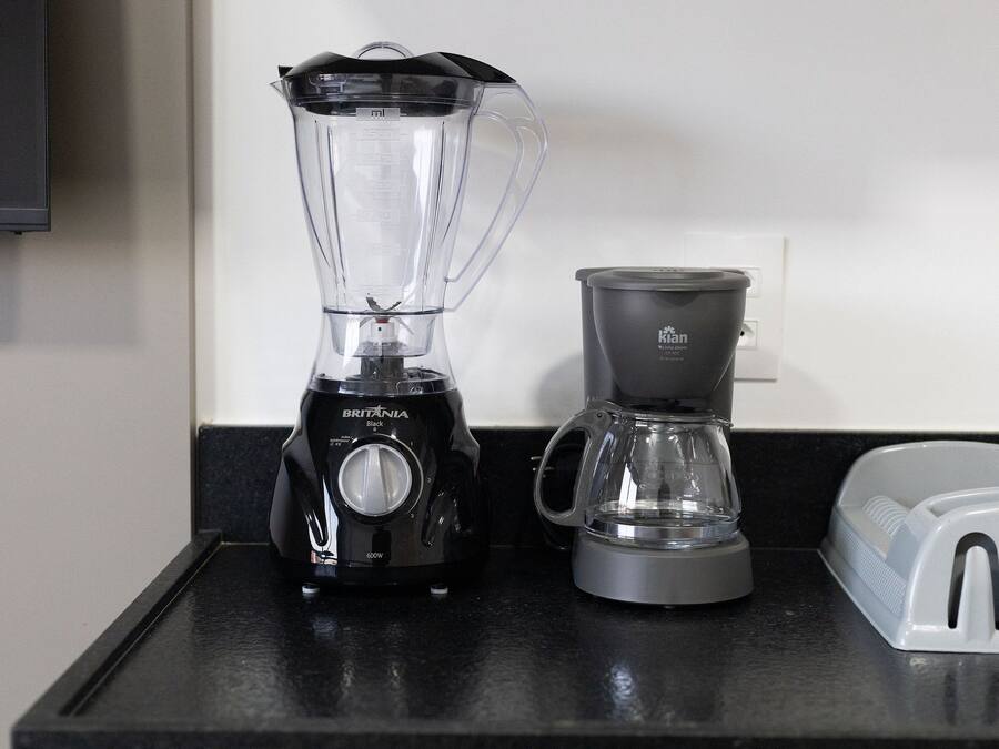 Una encimera de cocina con una licuadora negra, una cafetera gris y un tostador blanco.