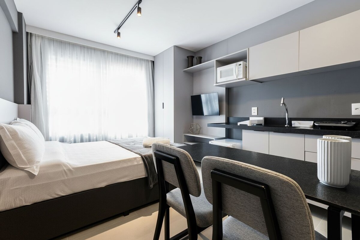 Une chambre d’hôtel moderne équipée d’un lit, d’une table à manger avec des chaises, d’un coin cuisine avec un four à micro-ondes et d’une télévision.