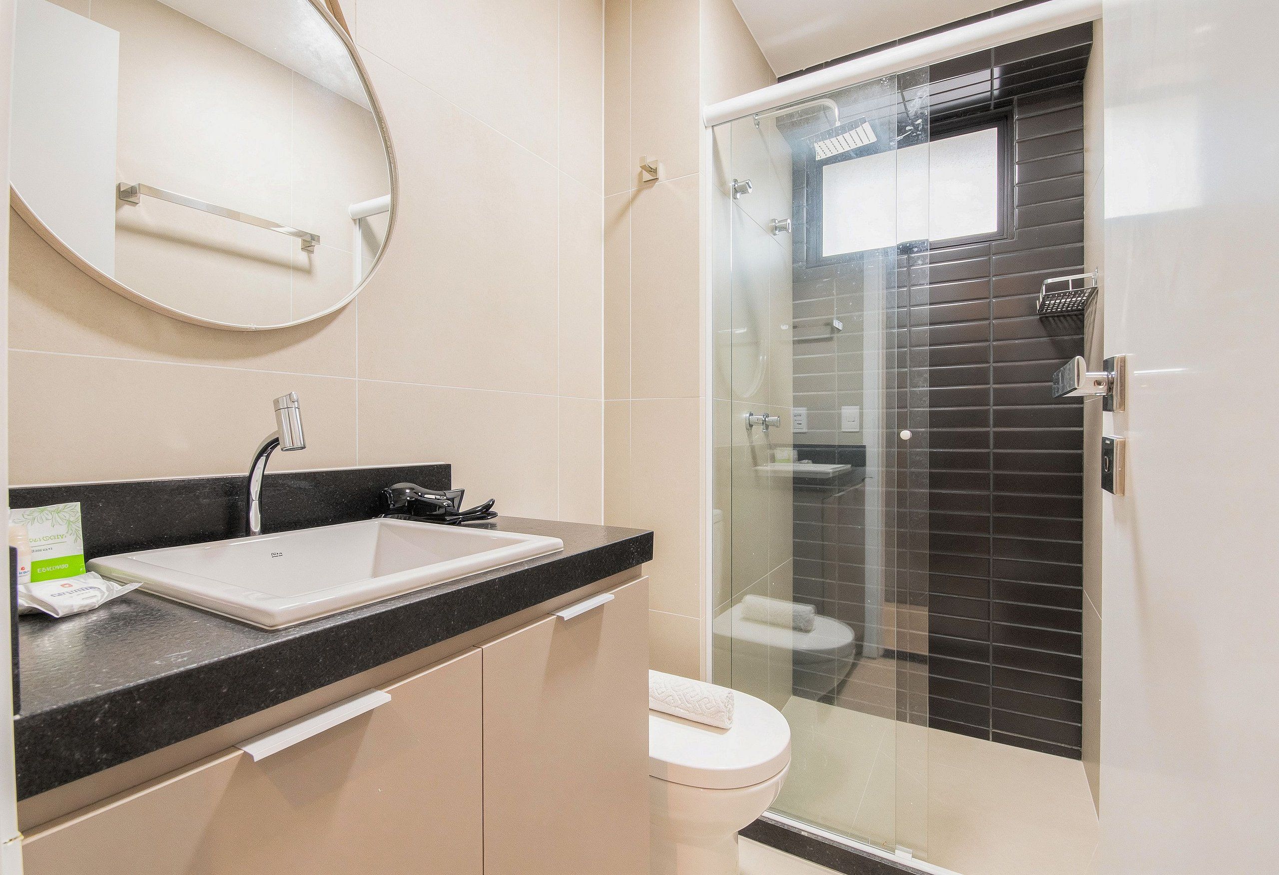 Un baño moderno con ducha envuelta en vidrio, un lavamanos blanco y una encimera negra.