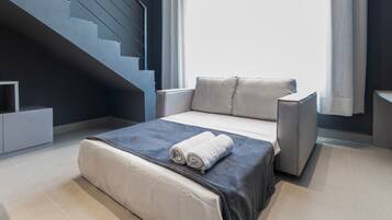 Un dormitorio moderno con una cama, un sofá gris, una escalera y un ventanal con cortinas.