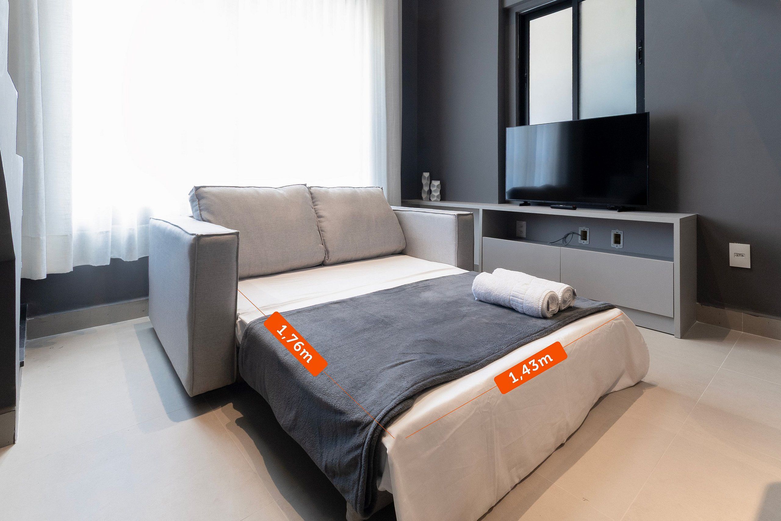 A modern bedroom with a bed measuring 1.76m by 1.43m, a TV above the bed, and a window with curtains.