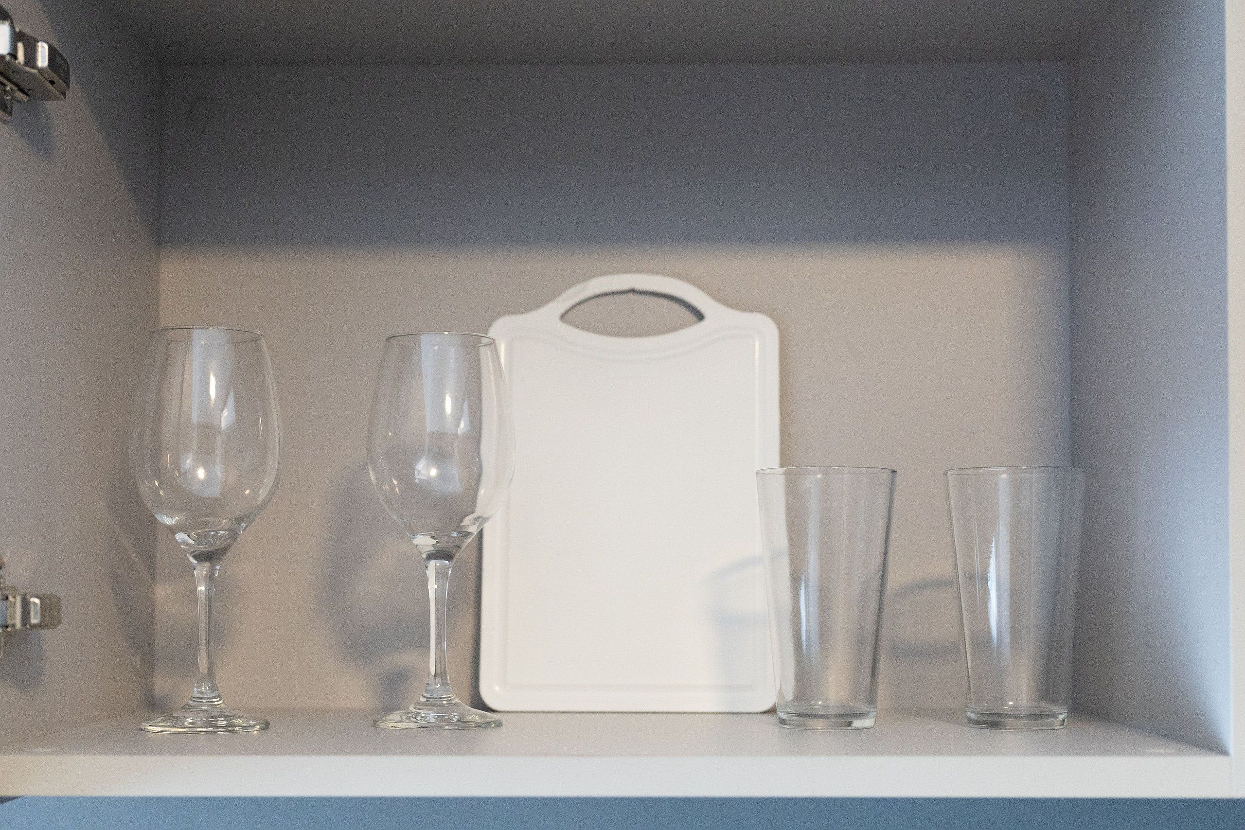Una estantería blanca con cuatro vasos transparentes y una bandeja blanca.